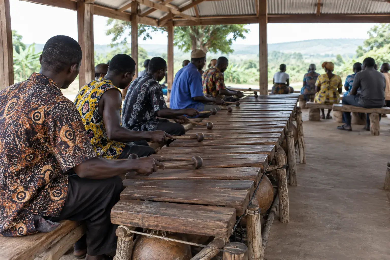 Des musiciens se répartissent les notes d’un grand xylophone en bois dans un pavillon ouvert.