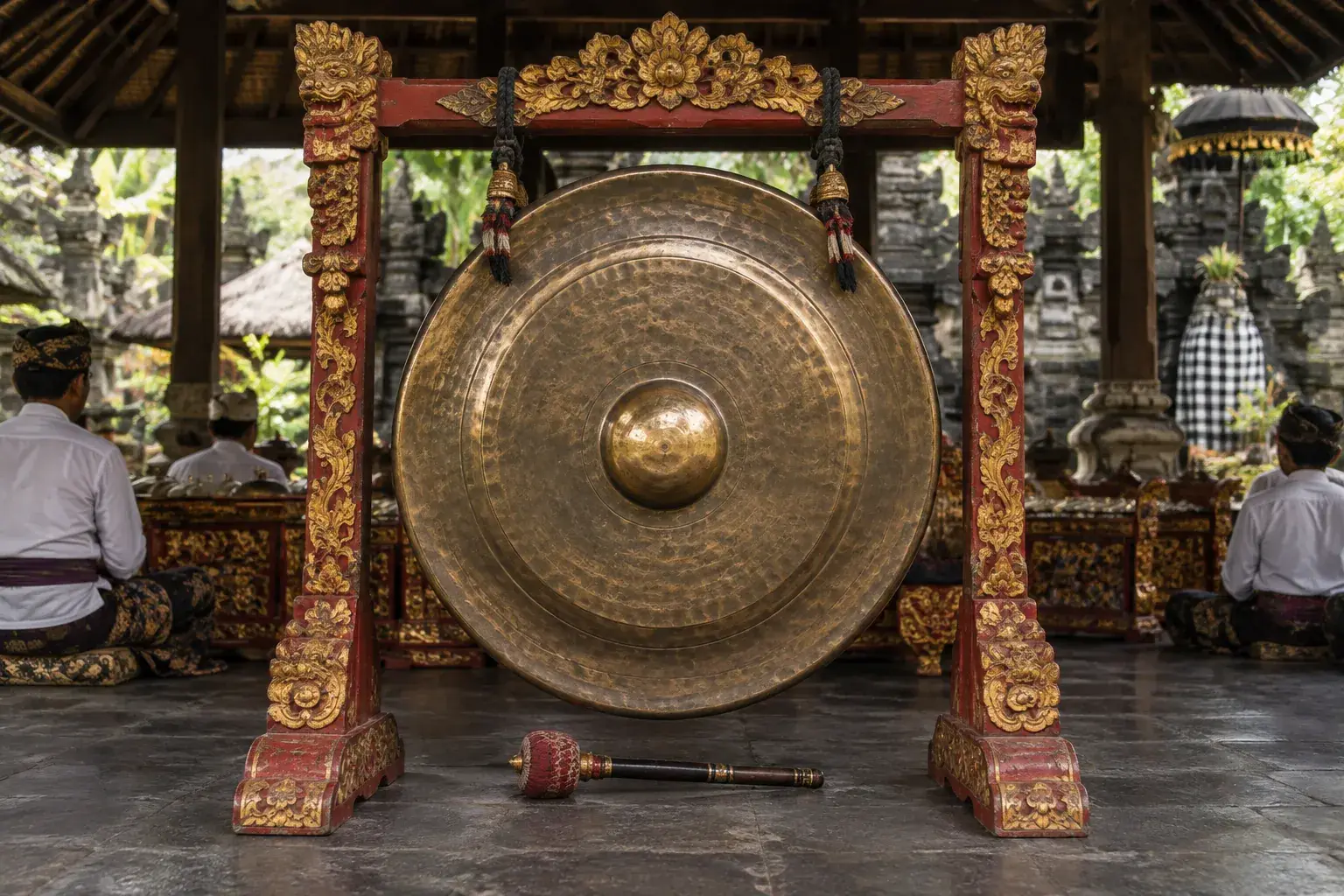 Un grand gong de bronze suspendu dans un support sculpté, avec son maillet posé au pied.