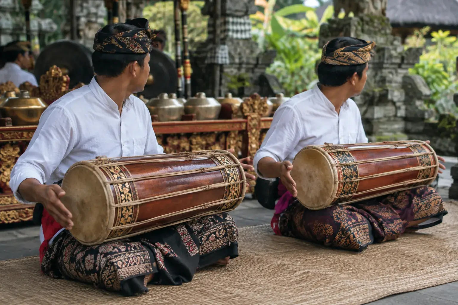 Deux tambours kendang en bois, lacés de cuir, reposent horizontalement sur les genoux des musiciens.